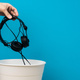 A hand tosses broken headphones into a trash can